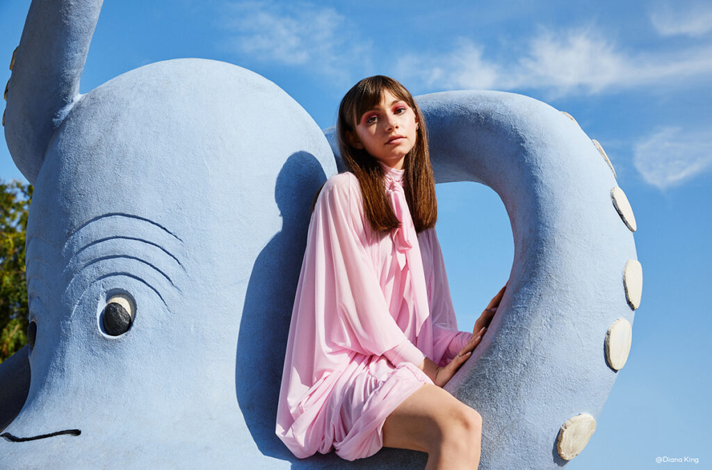 Model in a pink dress sitting on an octopus sculpture, photo by Diana King