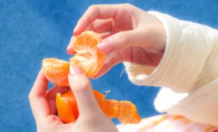 Hands peeling a tangerine against a blue background. Photo by Manyi Chan, edited in Capture One Pro