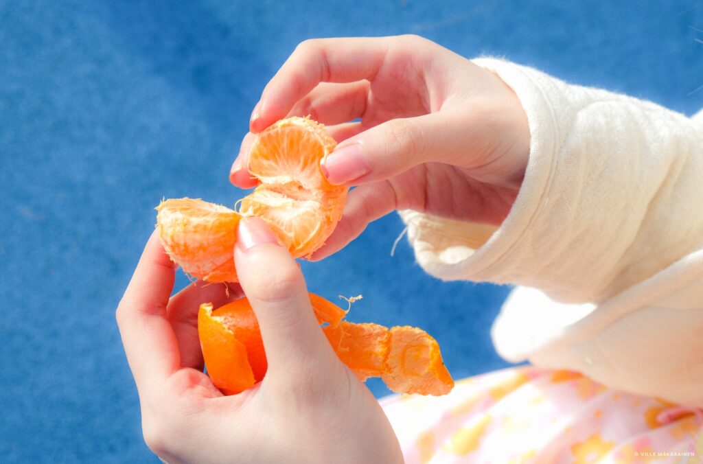 Hands peeling a tangerine against a blue background. Photo by photography student Manyi Chan, edited in Capture One Pro